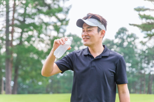 ゴルフ中に水分補給する男性