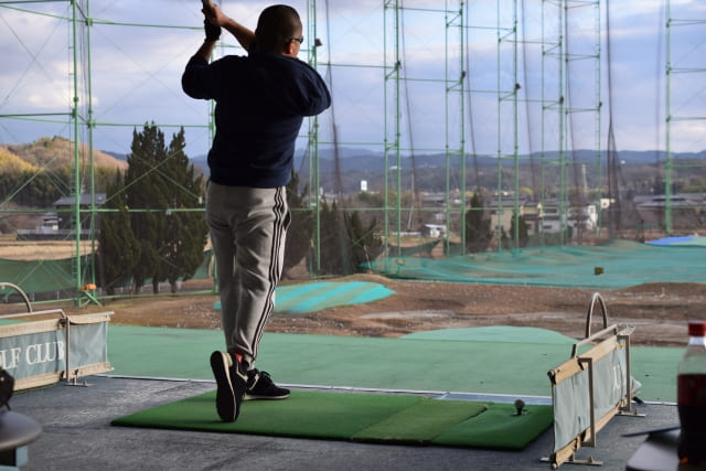 ゴルフ練習場で練習する中年男性